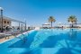 Una piscina con ombrelloni e palme intorno, sotto un cielo azzurro.