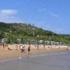 Spiaggia affollata con gente che gioca e colline verdi sullo sfondo.