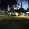 Campeggio notturno illuminato con roulotte e tende.