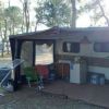 Camper con veranda aperta e sedie da campeggio sotto gli alberi.