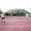 Persone che giocano a tennis su un campo all'aperto con palme sullo sfondo.