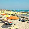 Spiaggia con lettini e ombrelloni gialli e arancioni su sabbia chiara.