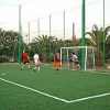 Una partita di calcetto in corso su un campo con erba sintetica e palme sullo sfondo.