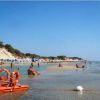 Spiaggia affollata con persone che si rilassano vicino all'acqua, bandiera di salvataggio visibile.