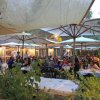 Ristorante all'aperto affollato, tavoli sotto ombrelloni.