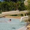 Un bambino si tuffa in piscina uscendo dallo scivolo, circondato da vegetazione.