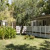 Bungalow con veranda tra alberi e prati verdi.