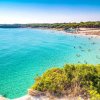 Spiaggia affollata con mare turchese e sabbia chiara.