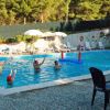 Bambini e adulti giocano in piscina, ombrelloni e sedie a bordo.