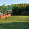 Un campo sportivo all'aperto con reti, circondato da alberi e una recinzione.
