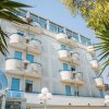 Edificio a più piani con balconi curvi e pareti bianche, circondato da alberi.