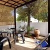 Un patio con sedie nere, tavolo di vetro, piante e una sdraio blu sotto una tettoia di canne.
