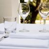 Tavola apparecchiata con bicchieri di vetro, tovaglioli bianchi e posate.