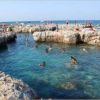 Persone nuotano in una piscina naturale rocciosa vicino al mare.
