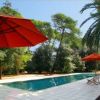 Piscina all'aperto con ombrelloni arancioni e sedie a sdraio, circondata da alberi.