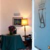 Una sala con tavolo coperto da tovaglia verde, fiori e lampada. Una porta con stemma è aperta.