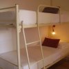 Letto a castello bianco con cuscini, illuminato da una lampada appesa.