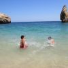 Due bambini giocano in mare vicino a scogli.