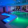 Piscina interna con illuminazione colorata e lettini bianchi.