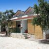 Bungalow bianco con tende di bambù, terrazza, alberi su strada di pietra.