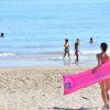 Persona sulla spiaggia con materassino rosa.