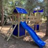 Area giochi con scivolo blu e struttura di legno.