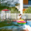 Bambini che giocano in una piscina, circondati da recinzioni bianche e piante.