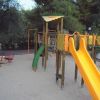 Parco giochi con scivolo arancione e altalene su sabbia.