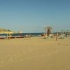 Spiaggia sabbiosa con ombrelloni e pedalò, isola all'orizzonte.