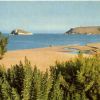 Spiaggia con vegetazione, mare e due isole in lontananza.