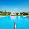Piscina limpida all'aperto circondata da ombrelloni e prato verde, cielo blu.