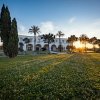 Edificio bianco con archi, alberi al tramonto su prato fiorito.