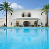 Grande villa bianca con piscina in primo piano e palme ai lati.