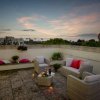 Terrazza con sedie di vimini, candele, cuscini colorati e bottiglia di vino al tramonto.
