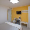 Camera luminosa con pareti gialle, TV, scrivania, minibar, armadio e letto con coperta chiara.