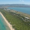 Vista aerea di una lunga spiaggia con acqua turchese, vegetazione e un lago.